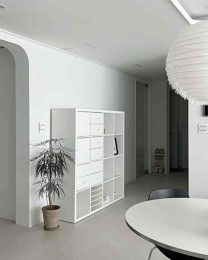 White and natural toned living room with plant and storage bookshelf, featuring modern and minimal interior design