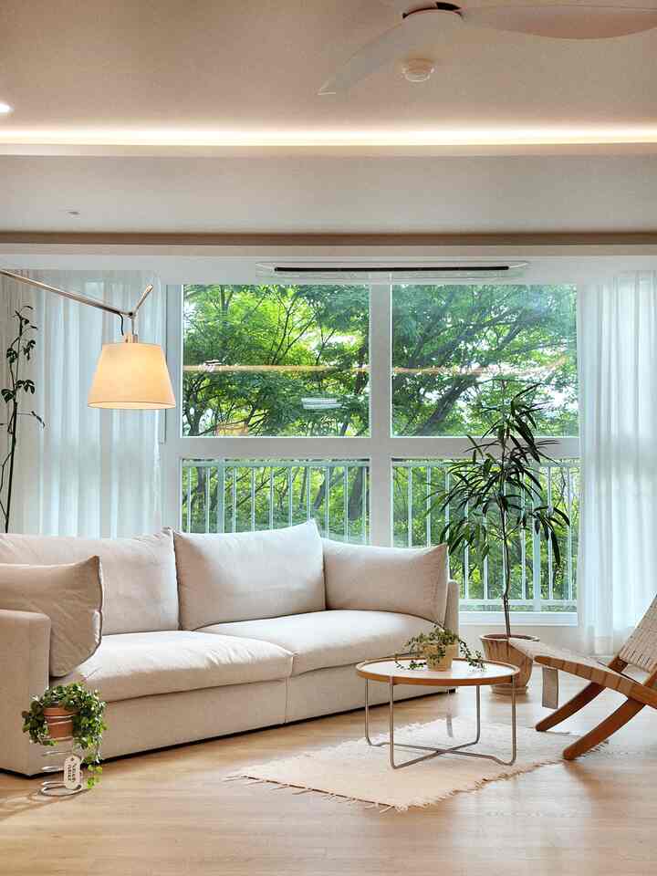 Bright beige and light brown toned living room featuring large sofa, round coffee table, and various plants for a natural atmosphere