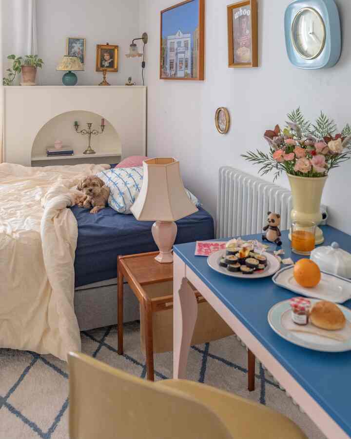 White and blue toned bedroom featuring a small dog on bed, blue table with food and decor, creating a cozy atmosphere