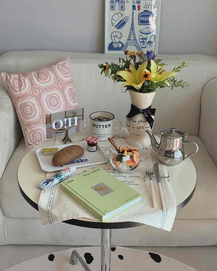 白とピンクのトーンのリビング、丸テーブルの上のフレンチ花瓶と花、ソファと額装アートが調和したモダンでヴィンテージな印象的な空間