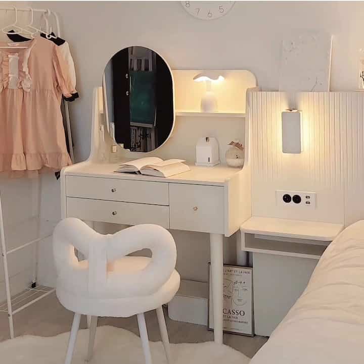 Bright white-toned kids' room featuring a wooden vanity with round mirror, soft vanity chair, and cozy bedroom ambiance