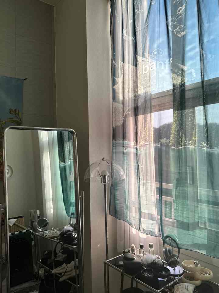 Quiet interior space featuring transparent and silver metal furniture with teal chiffon curtains softly filtering sunlight