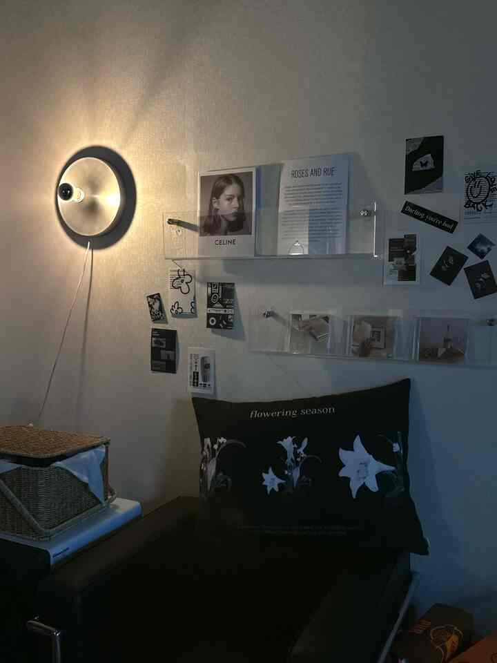 A softly lit studio apartment featuring a black leather sofa, wall-mounted posters, and transparent acrylic shelves