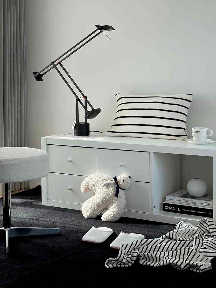 Modern living room in white and black tones featuring a stool and storage unit with a clean arrangement