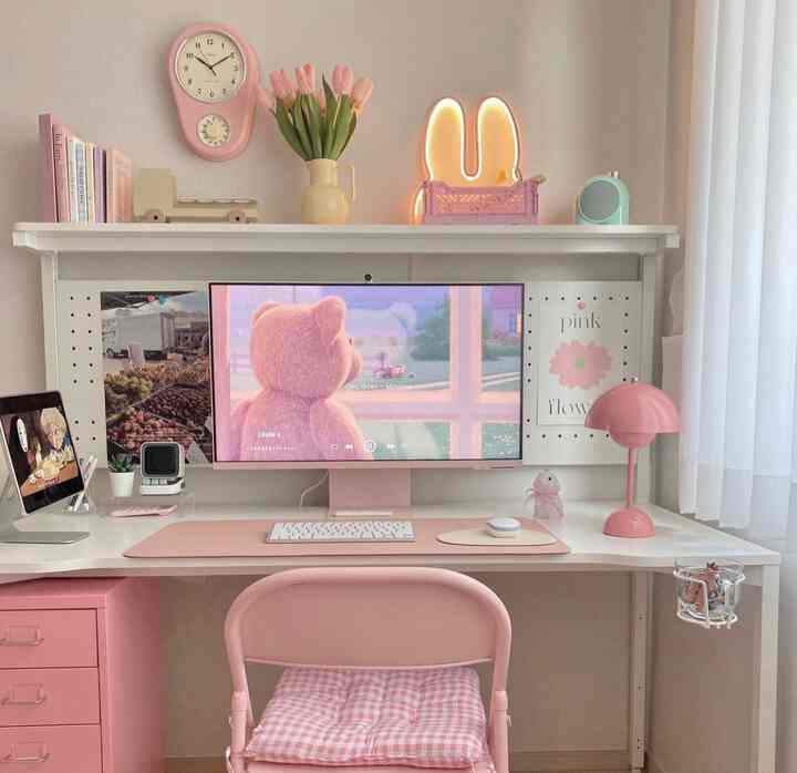 Pink and white toned home office featuring desk, chair, computer, and cute pink accessories with a simple interior style