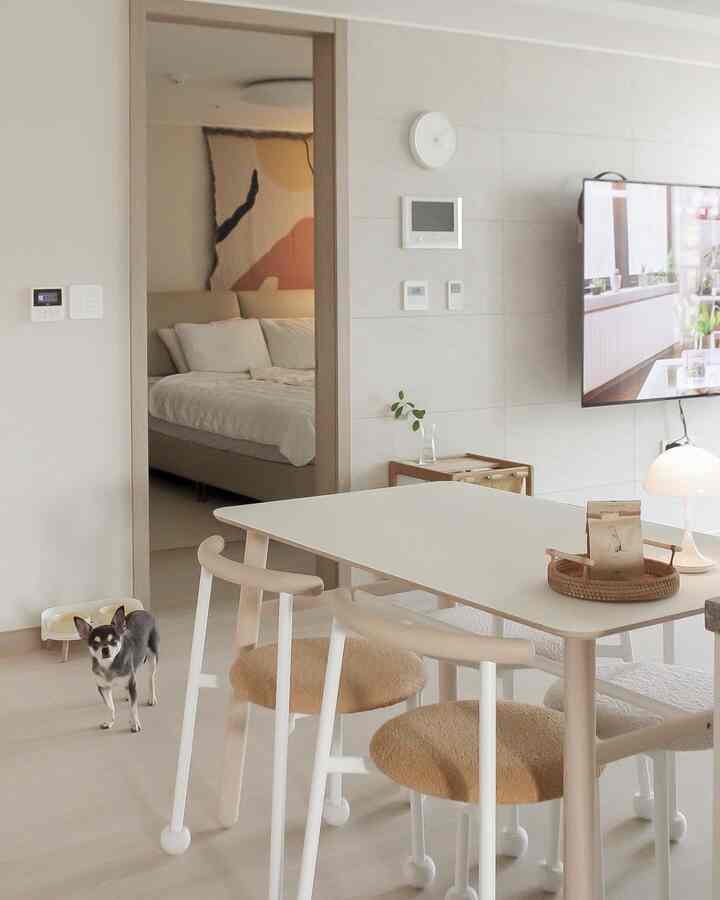 白とベージュの色調のリビングルームとダイニングテーブル、ペットの犬とフードボウルが置かれたナチュラルモダンな雰囲気のインテリア