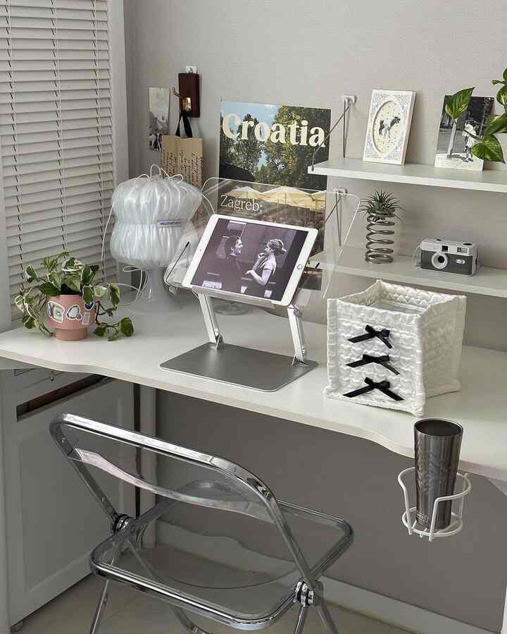 ホワイトとシルバーのトーンが調和したホームオフィスのデスクスペース、透明な読書台とリボン付き収納バスケットが配置された洗練されたモダンなインテリア
