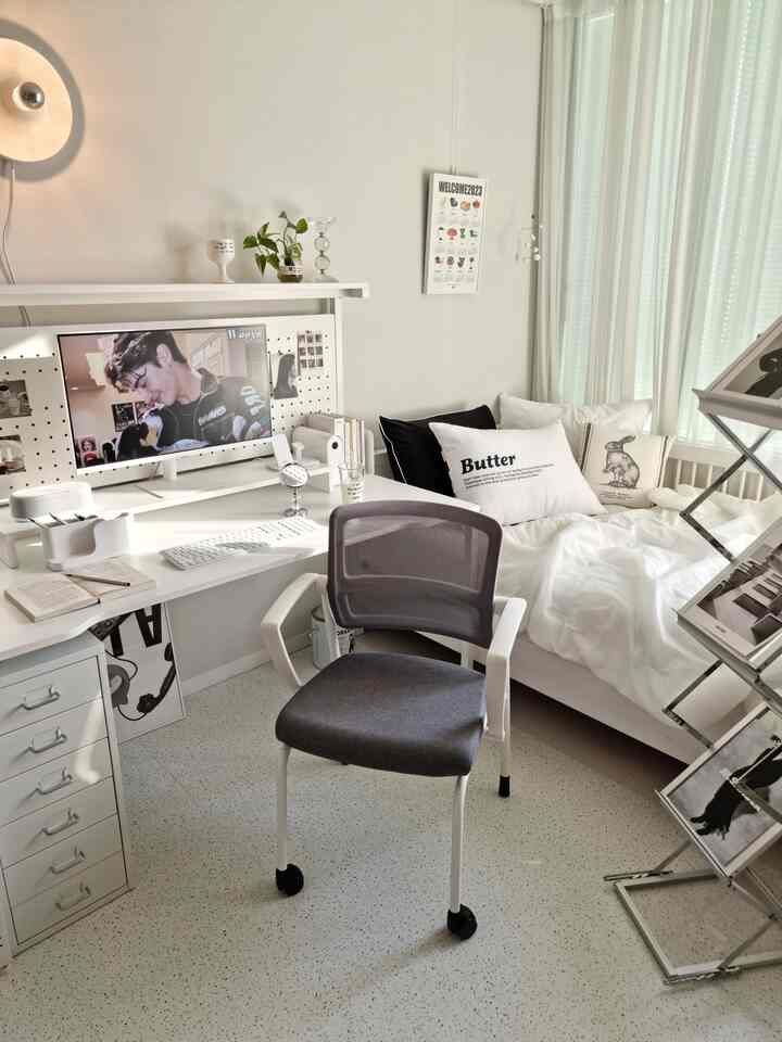 A clean, simple white and gray toned bedroom combined with a home office featuring a desk, chair, and wall lamp