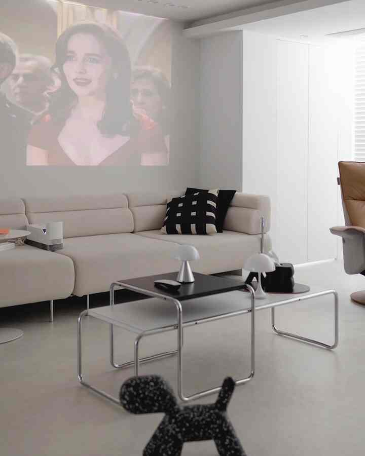 White and beige toned living room featuring mid-century modern sofa, coffee table, and home cinema screen with a modern atmosphere