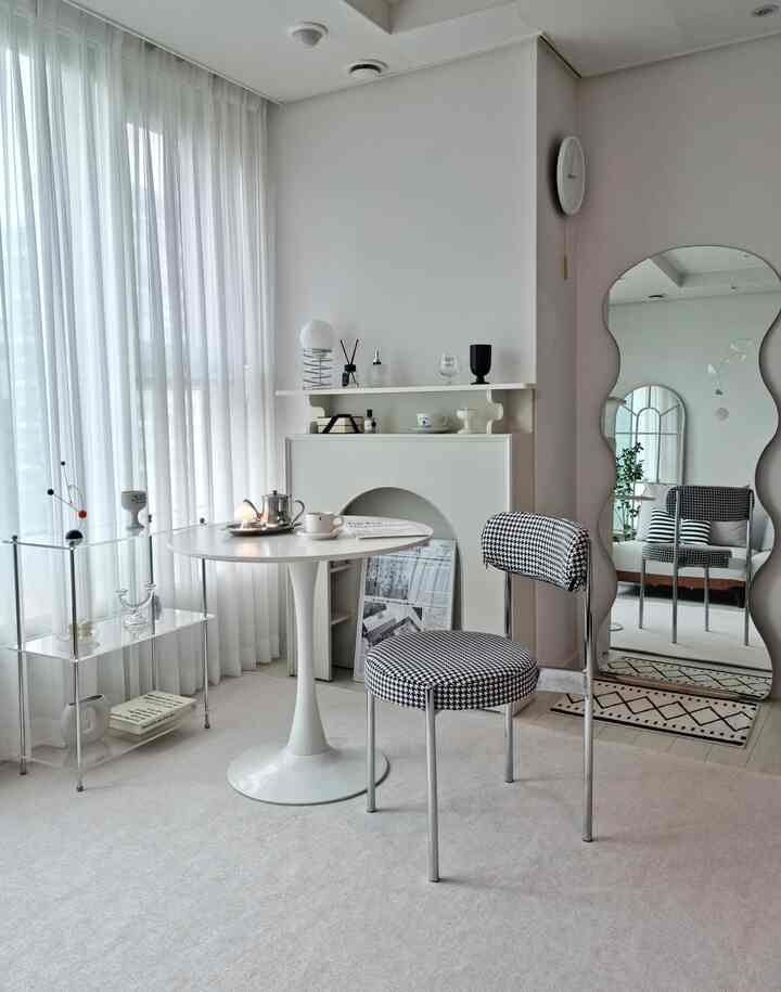 Bright white-toned living room featuring a white round table and modern patterned chair at the center with a minimalist feel