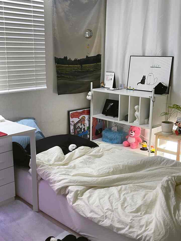 ホワイトとモノトーン調のワンルーム寝室、ベッド、デスク、本棚が配置された落ち着いた空間