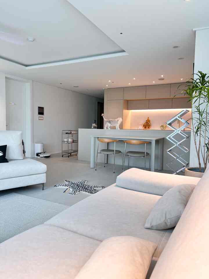 Ivory and white toned living room and kitchen featuring simple modern sofas and wooden dining chairs in a clean interior