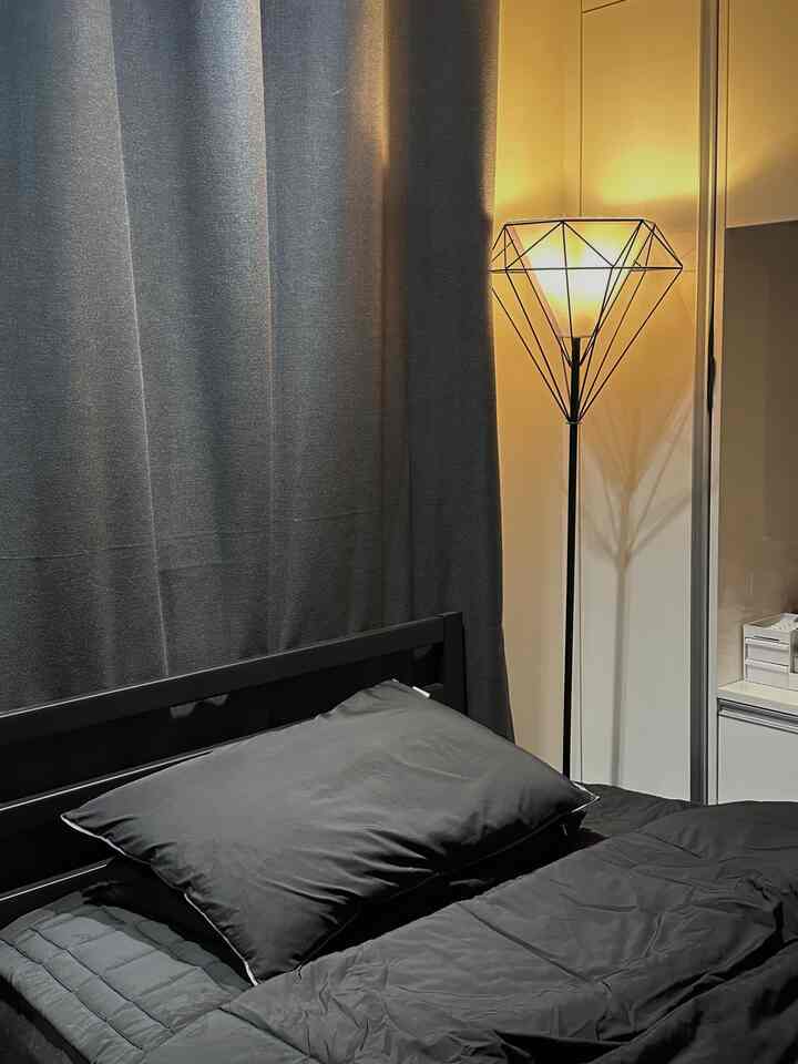 Black-toned bedroom featuring a diamond-design floor lamp and blackout curtains, creating a modern and calming atmosphere