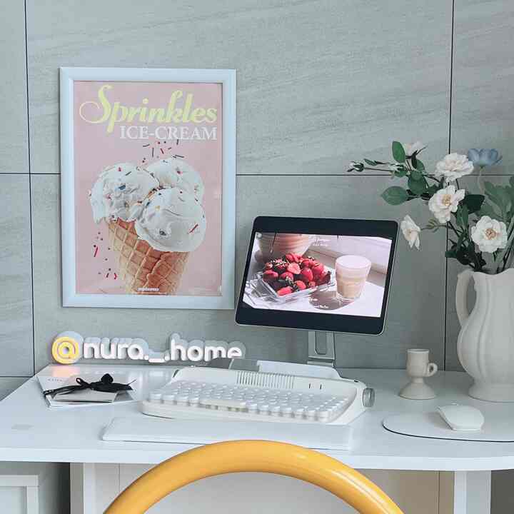 Minimalistic home cafe workspace in white and pastel tones featuring a desk, tablet, vase with flowers, and framed wall art