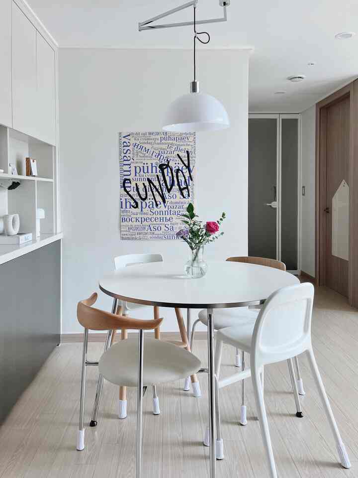 ホワイトトーンのダイニングルーム、丸いダイニングテーブルと多様なデザインのチェア、壁にはレタリングポスターとペンダントライトが配置された整ったおうちカフェ空間