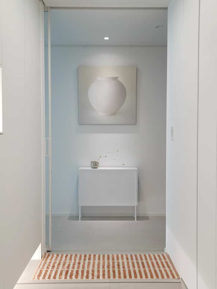 White-toned entrance space featuring a console table with minimal decor centrally placed, creating a clean and modern atmosphere