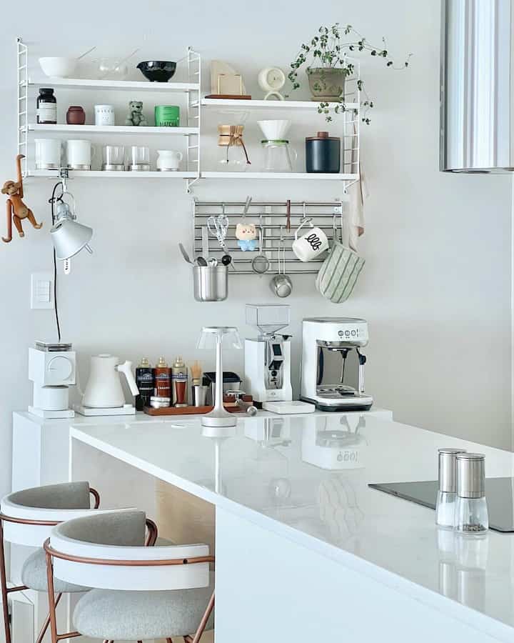 White-toned studio kitchen with a minimal style featuring a coffee machine and stools in a clean home cafe setup