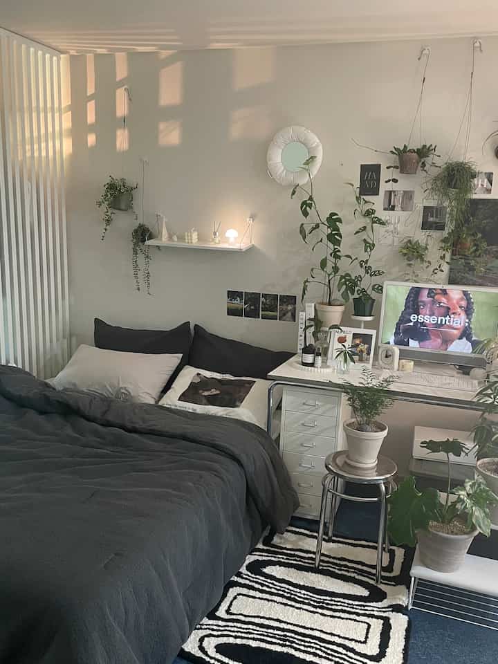 Modern bedroom in black and white tones featuring a bed, desk, and various plants with a cozy and stylish atmosphere
