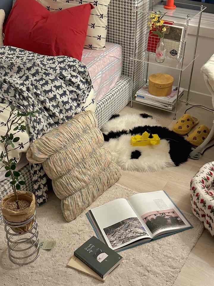 ナチュラルトーンのコンパクトな寝室、ベッドとパターンのクッション、パンダのラグが配置された雰囲気のある空間