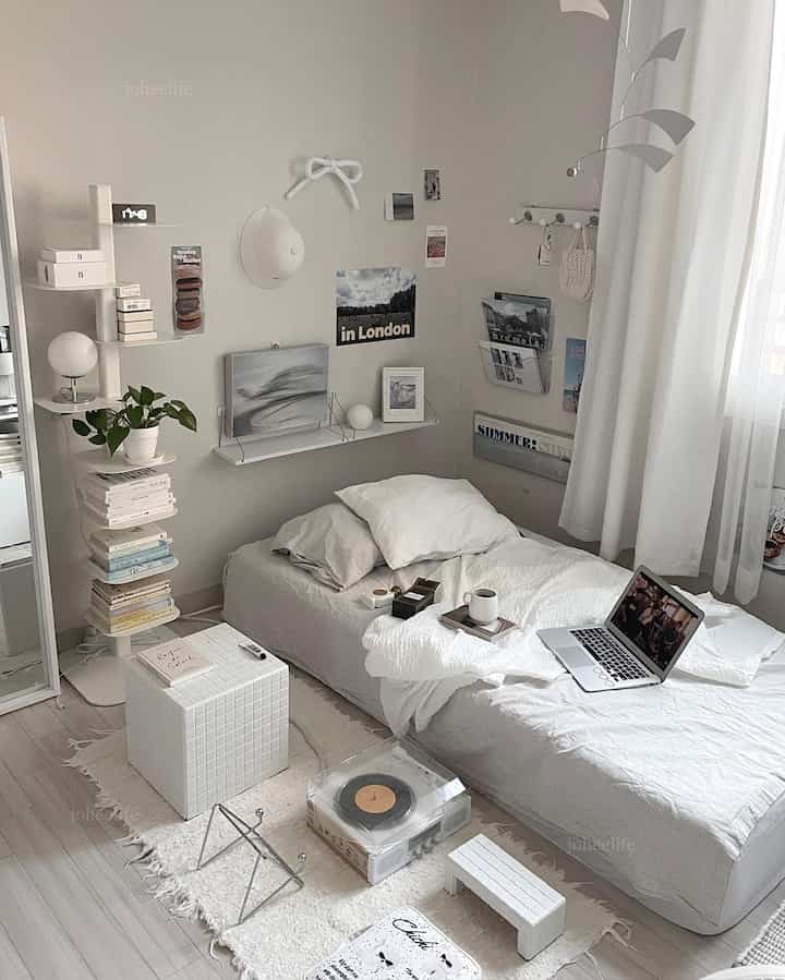 White and natural toned studio bedroom featuring a small shelf, rug, and laptop with a minimalistic atmosphere