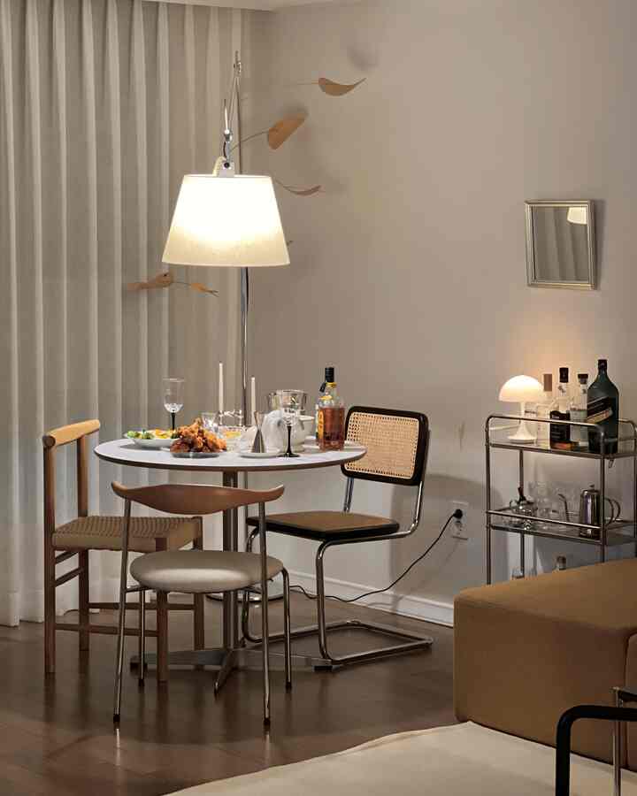 白い壁と茶色の木製床が調和するリビング兼ダイニング空間に、ミッドセンチュリーモダンスタイルの丸テーブルと様々な椅子が配置された落ち着いたインテリア