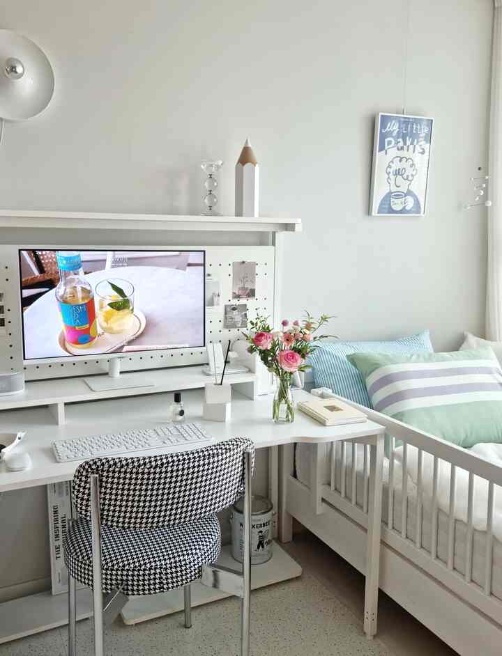明るいホワイトトーンの子供部屋、中央にデスクとコンピューターモニター、デスク上に透明な花瓶とピンクの花が配置された清潔感のあるインテリア