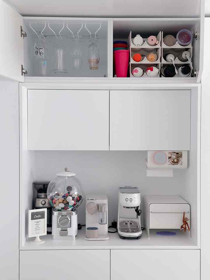 White-toned home cafe space featuring coffee machines, capsule organizer, and bottle drying rack with neat and organized interior