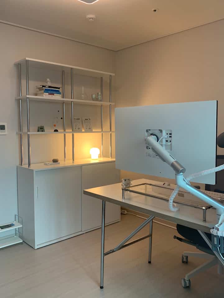 白とシルバーの調和が美しいホームオフィス空間、シンプルなデスクとクロム製の棚、ムードランプが配置されたモダンなインテリア