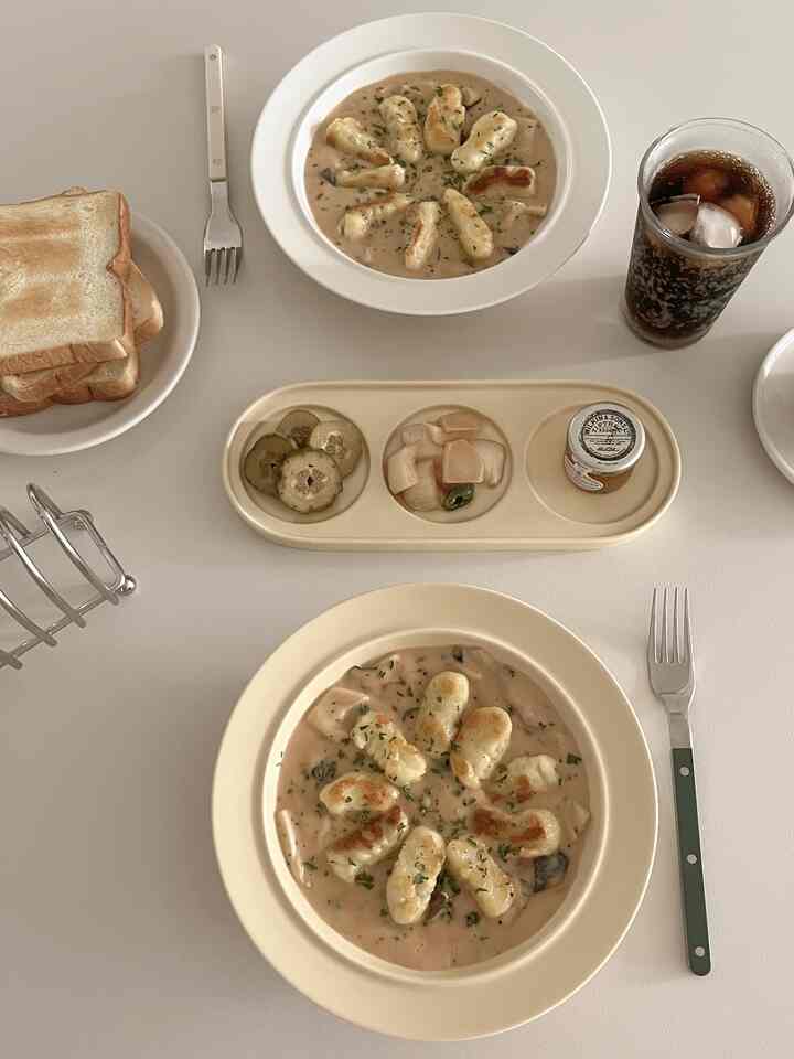 ホワイトトーンのダイニングテーブルにパスタボウル、トースト、ドリンク、カトラリーが整然と配置された温かみのあるホームブランチ空間