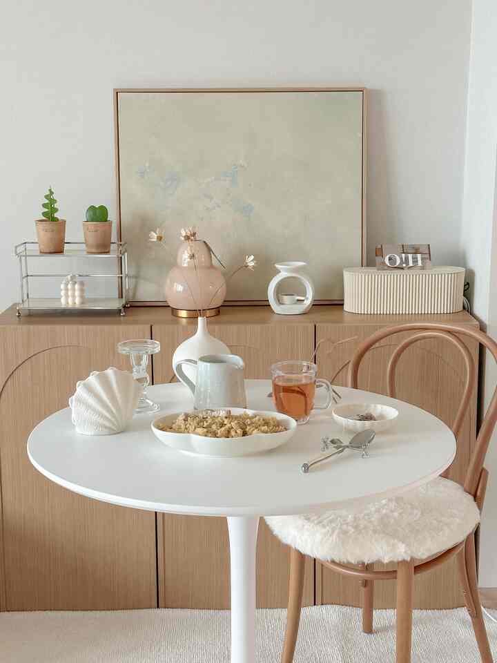 A cozy home cafe space with harmonious white and wood tones, featuring a round dining table and chair in a simple interior