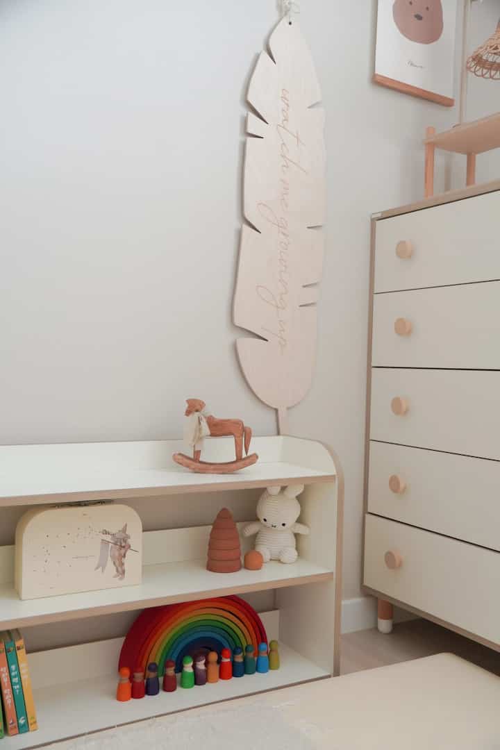 White and beige wood-toned kids' room featuring toys, low shelves, and a chest of drawers creating a cozy atmosphere