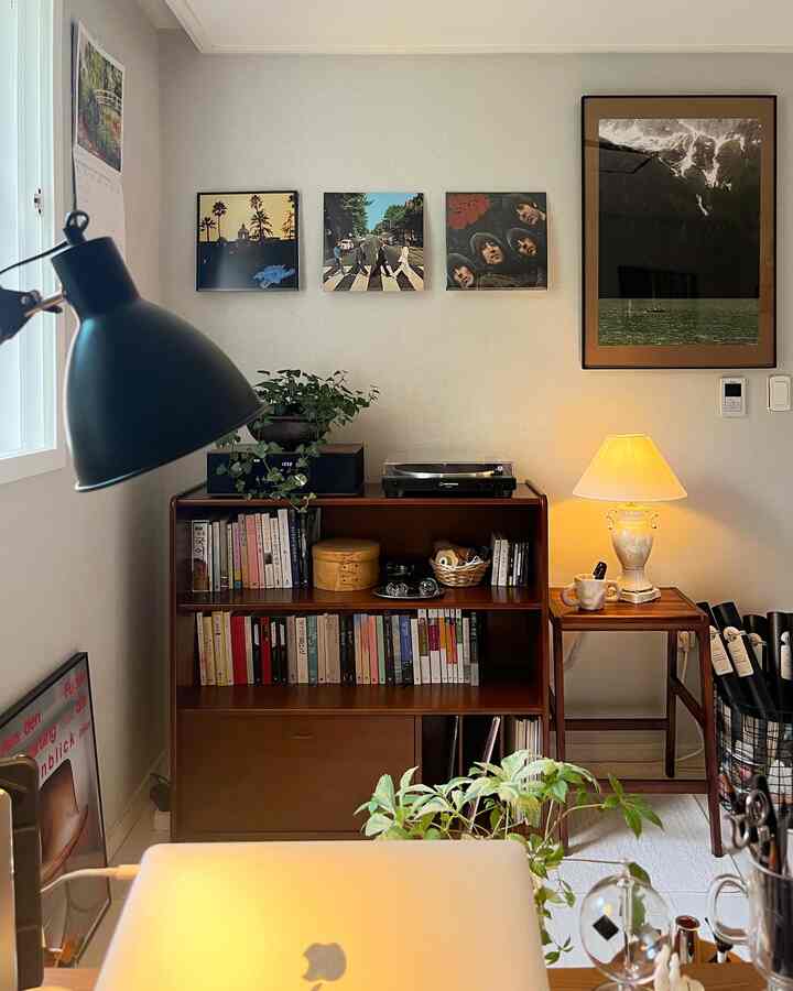 ブラウン調のホームオフィス、木製の本棚とポスター、テーブルランプ、植物が配置された雰囲気のあるインテリア