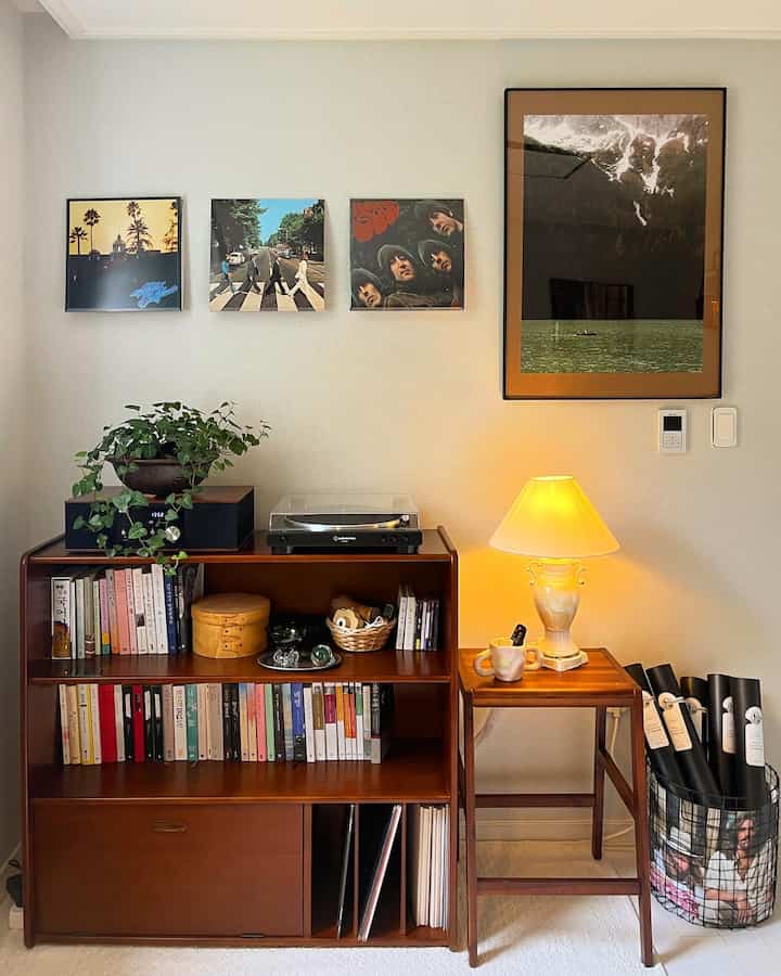 Cozy corner living room with natural wood furniture and posters, featuring a table lamp and plant for warm atmosphere