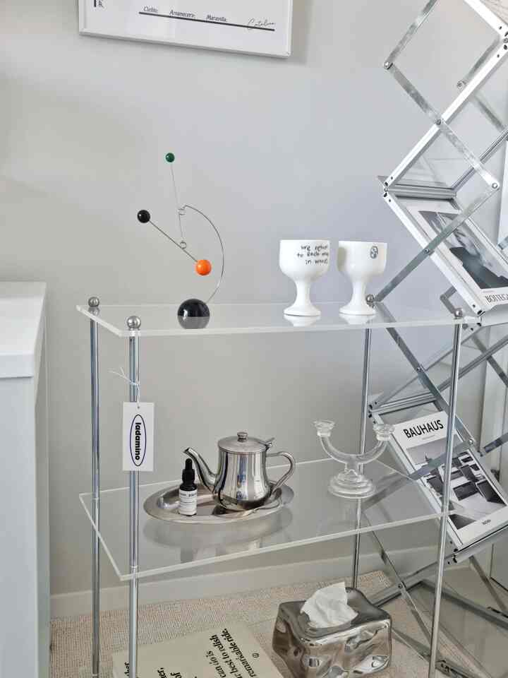 Mid-Century Modern space with white and silver tones featuring an acrylic modular shelf, goblet cups, and stainless steel tray in a clean, stylish setting
