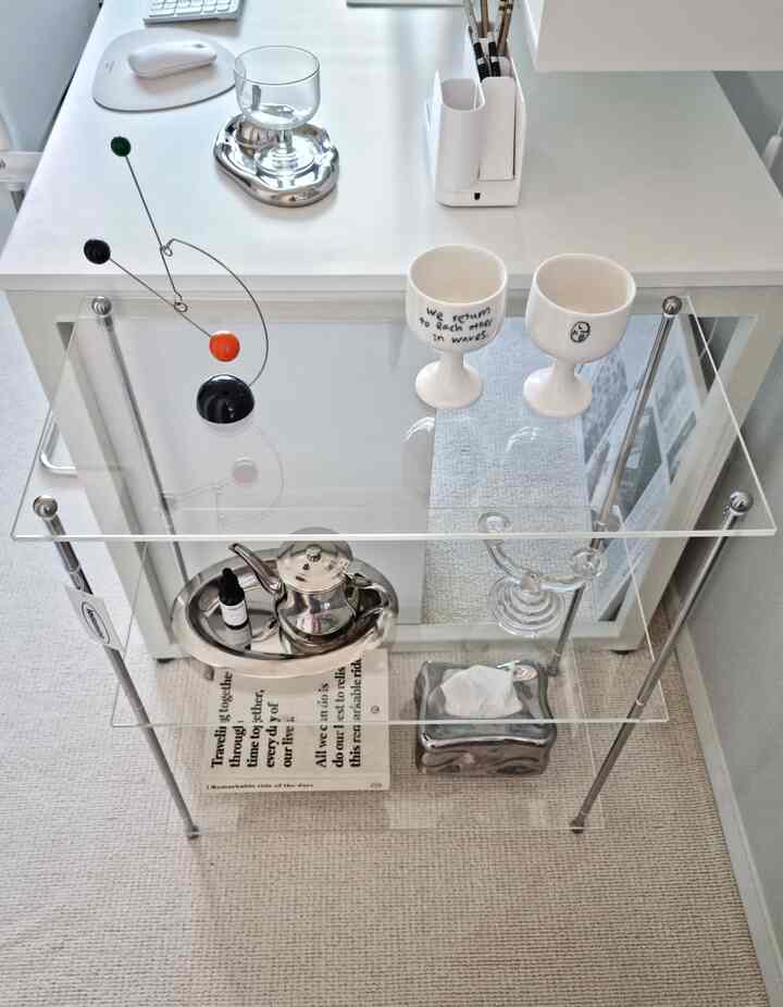 白と透明素材のワンルーム作業スペース、モダンなステンレス製オブジェと小物がアクリル棚に整然と配置された雰囲気のあるインテリア