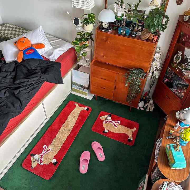 木目調と緑のカーペットが印象的な居心地の良い寝室、犬柄のラグとピンクのスリッパが配置されている。