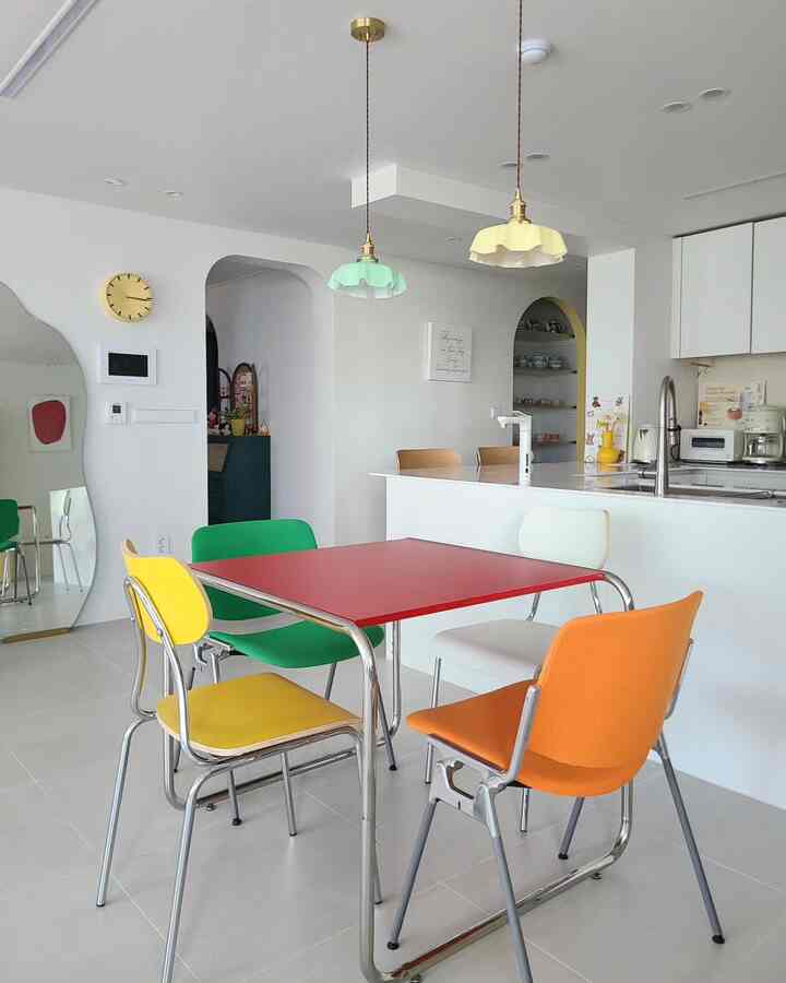 ホワイトを基調としたキッチンとダイニングルーム、赤いダイニングテーブルとカラフルな椅子が配置された明るくモダンな空間