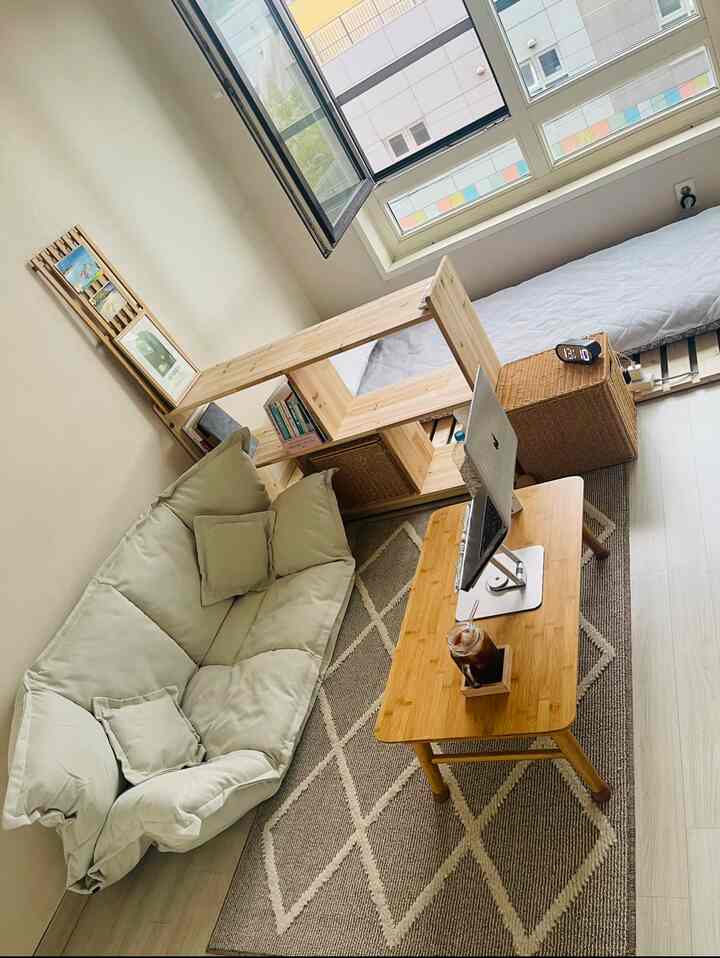 ナチュラルな木目調とベージュの小さい一人暮らしの部屋、ソファと低いテーブル、本棚が配置された落ち着いた在宅勤務空間