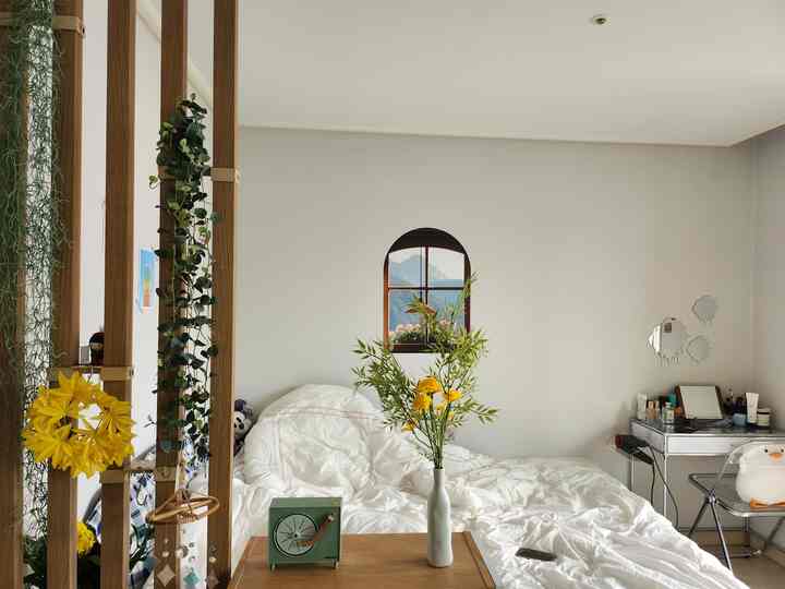 白と木目調が調和したワンルームの寝室、中央にクイーンベッドと右側に化粧台が配置された雰囲気のある空間