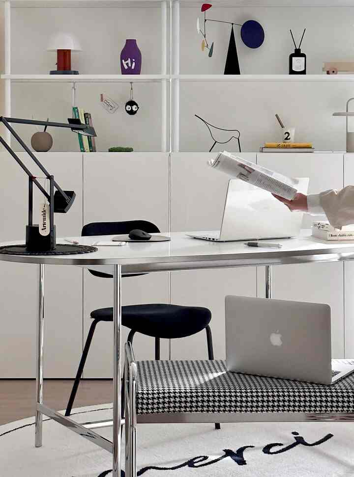 白い壁とシルバーの金属製テーブルが中央に配置されたモダンなホームオフィス、黒い椅子とミニマルな装飾品が整ったきれいな空間