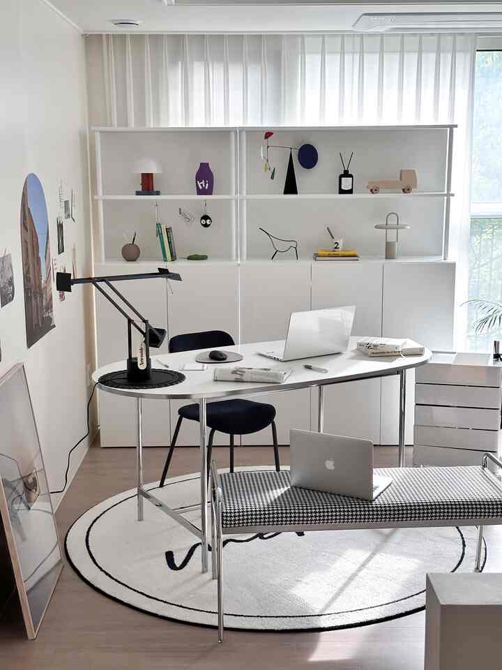 白と黒のトーンのホームオフィス、中央に丸いデスクと本棚が配置された印象的なシンプルモダンなインテリア