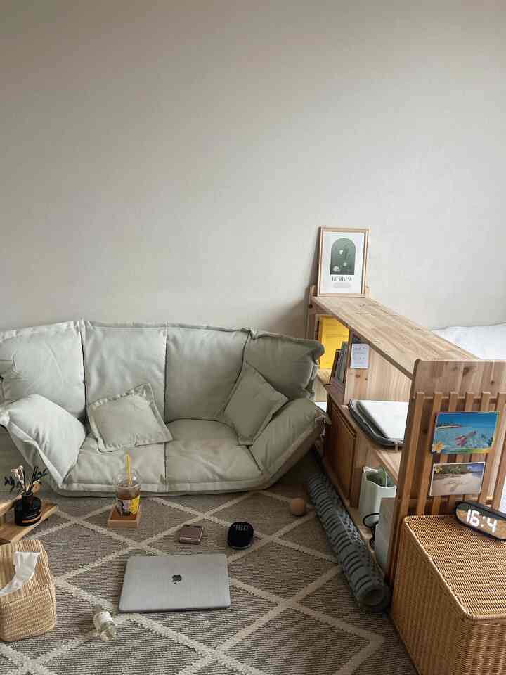 ベージュの壁と木製デスクが配置された落ち着いた一人暮らし用リビング、柔らかなグリーンのソファが温かな雰囲気を演出