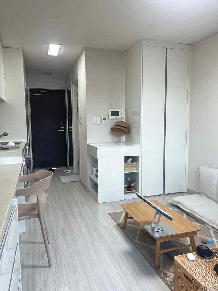 白とベージュのトーンで統一されたワンルーム、シンプルでコンパクトなレイアウトのキッチンとリビングが配置された雰囲気のあるインテリア