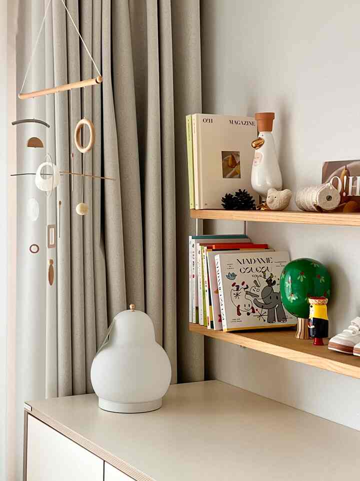 Natural toned baby room featuring wooden shelves, a mobile, and soft lighting creating a cozy and tidy space