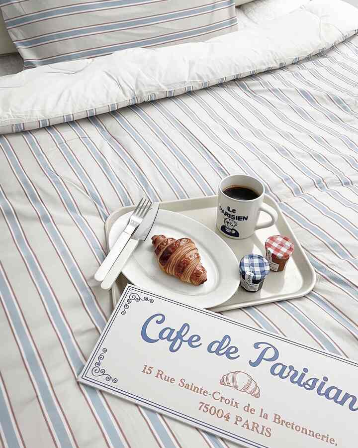 青と白のストライプ柄寝具が配置された寝室、トレイにクロワッサンとコーヒーが置かれた雰囲気のあるインテリア