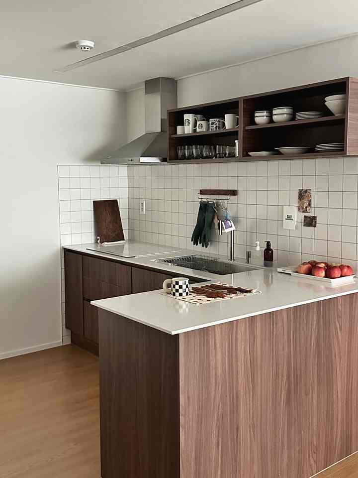 Minimal kitchen with white walls and wood-tone cabinets, featuring a kitchen island and open shelving in a tidy layout
