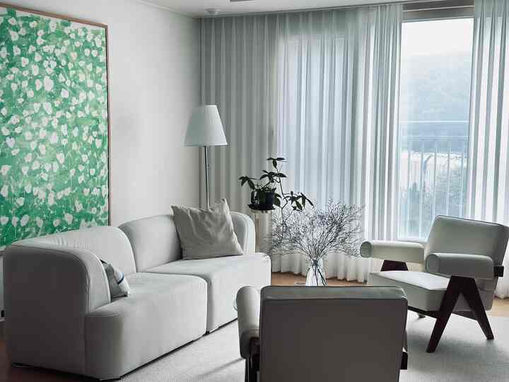 A white and green toned living room featuring a comfortable sofa, armchairs, and floor lamp in a natural modern setting