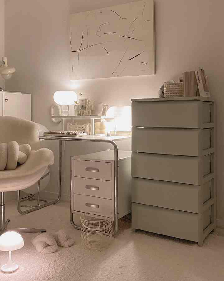 Bright white-toned bedroom featuring a minimalist desk, dresser, and cozy lighting in a clean interior