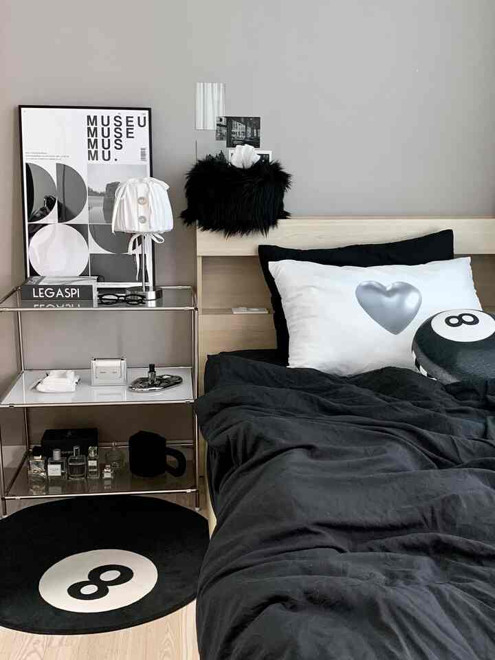 Monotone studio bedroom featuring black bedding, wooden bed frame, and an 8-ball motif rug with a modern vibe
