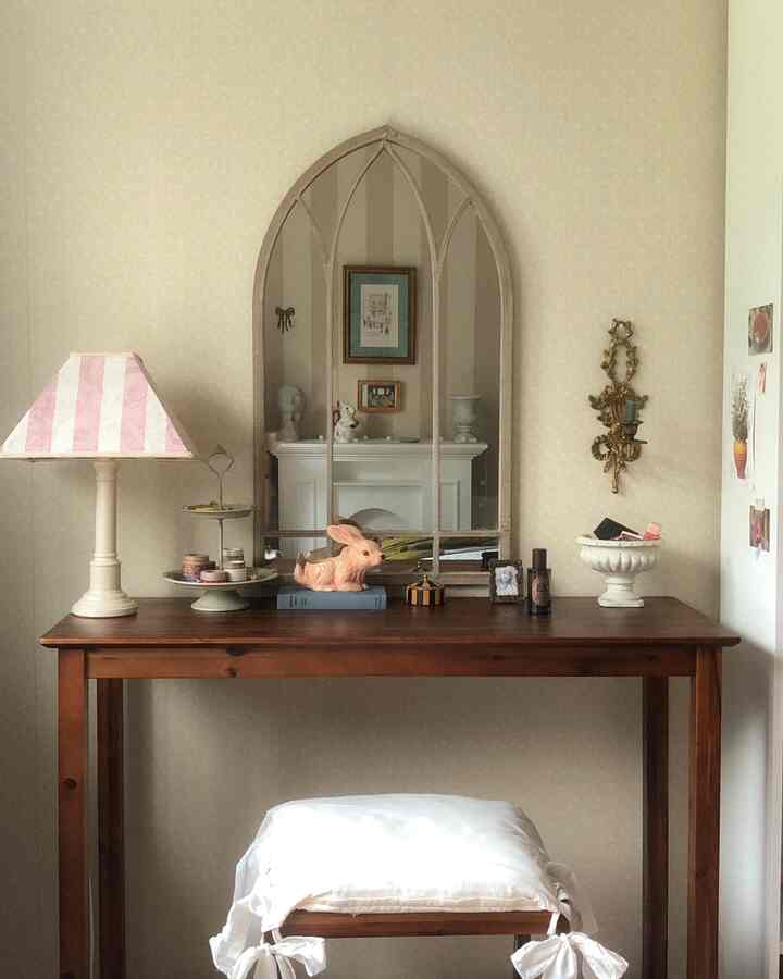 ベージュ色調の壁とアーチ型の鏡が配置されたヴィンテージスタイルの化粧台空間、木製のテーブルとスツールが温かみのある雰囲気を演出